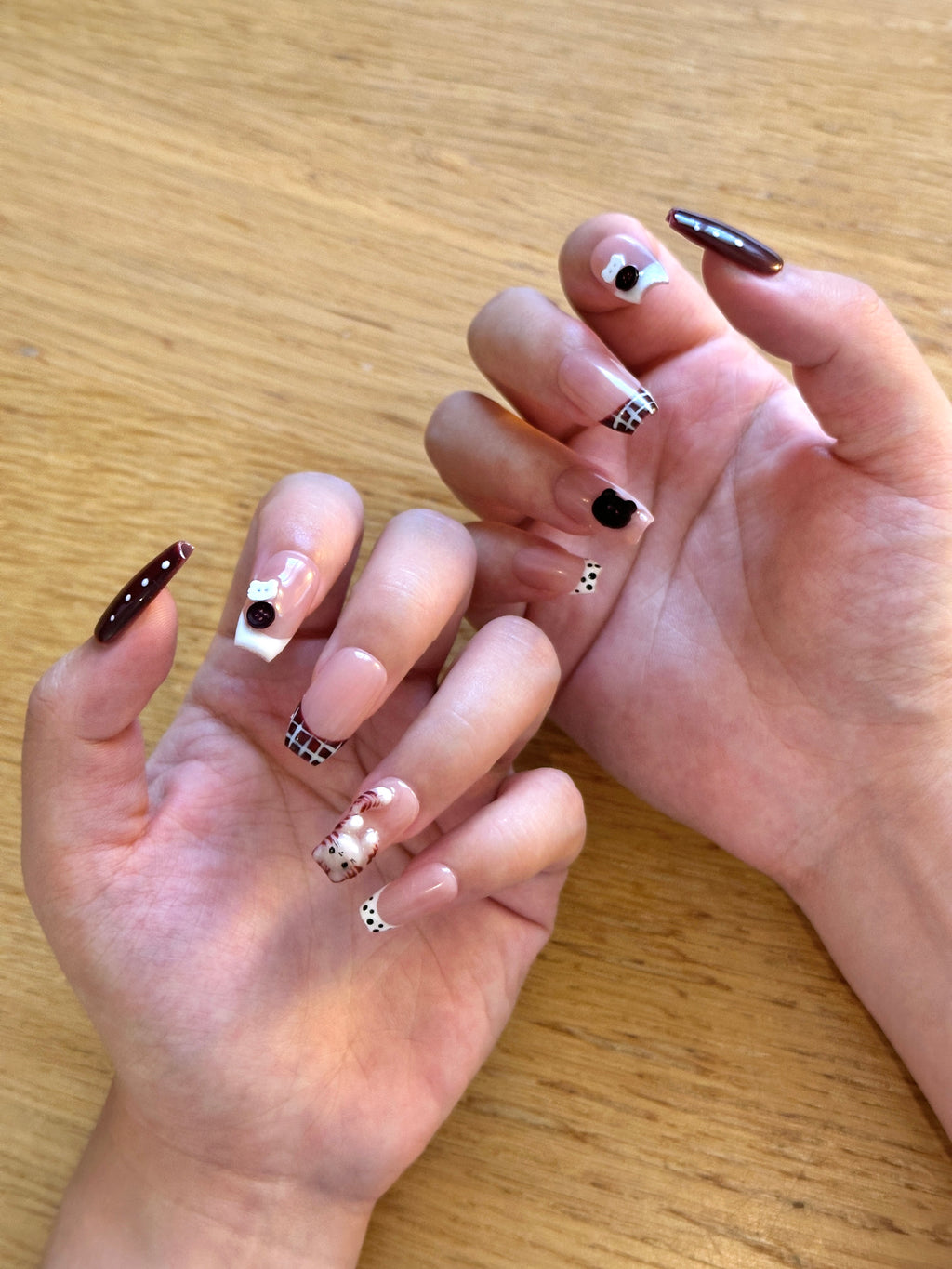 Close-up of hands with open palms, showing coffin press-on nails with 3D sculpted cat charm, dark espresso tips, plaid patterns, and polka dots