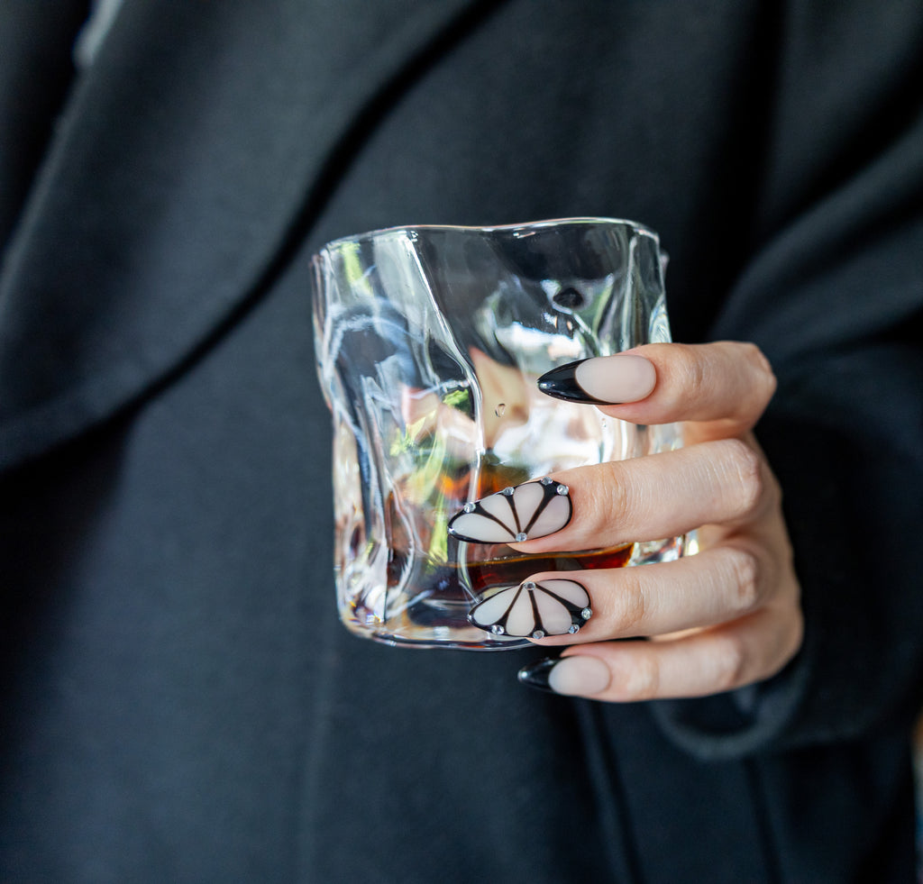 Close-up of hand wearing black butterfly French tip press-on nails in natural light