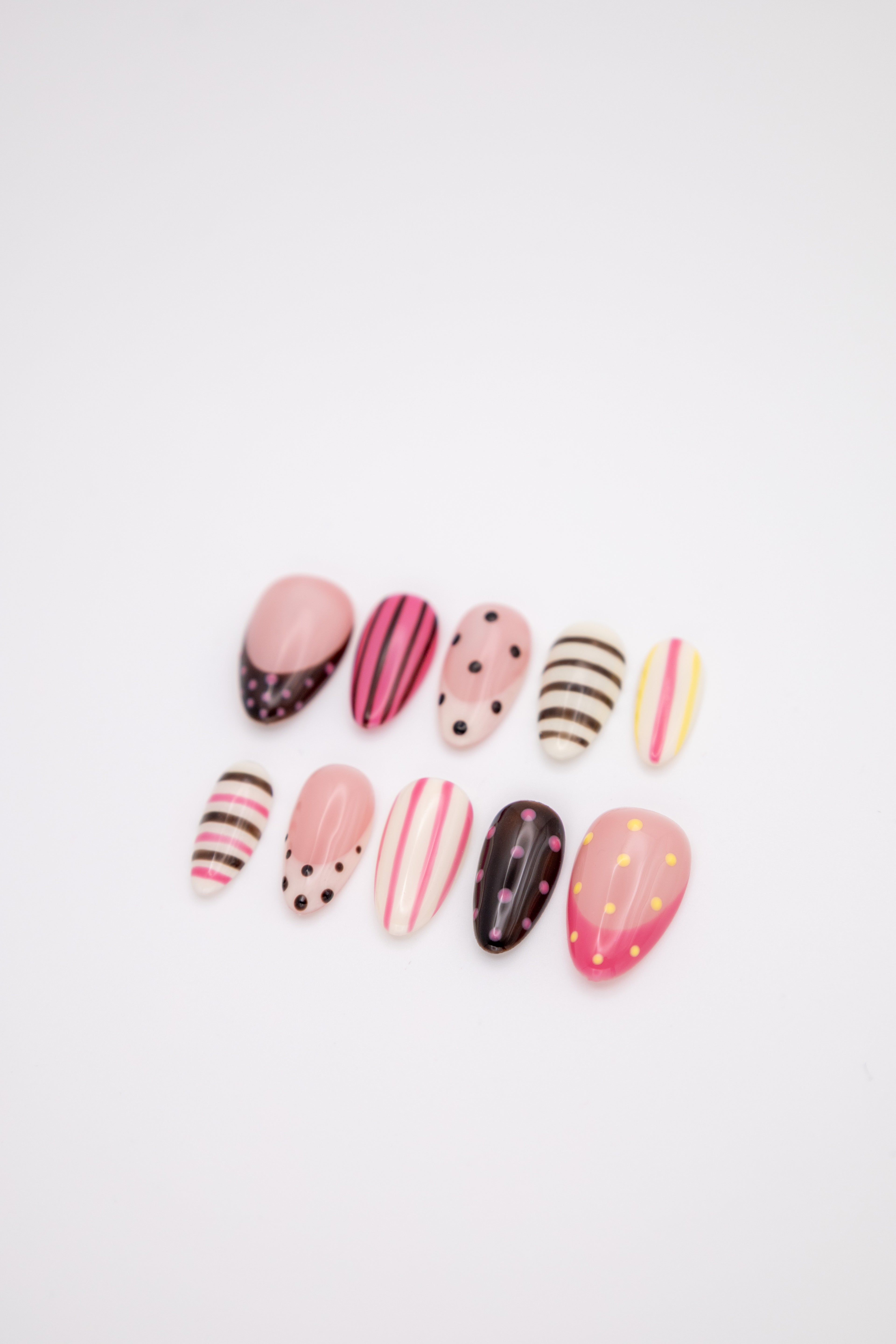 Flatlay of glossy almond press-on nails with colorful pink black polka dots and stripes designs