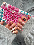 Hands posed in front of a pink mechanical keyboard, displaying oval press-on nails with glossy pink and black polka dots and candy stripe patterns
