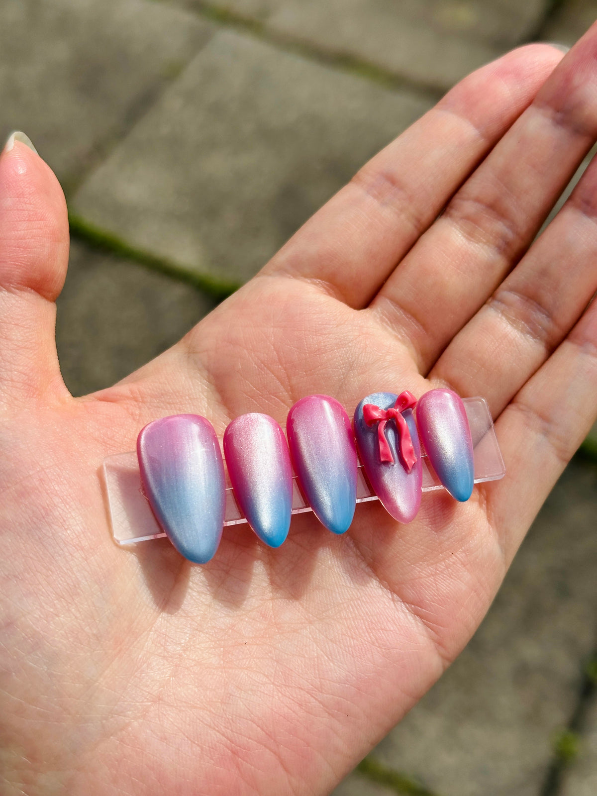 Close-up of pink blue gradient cat-eye almond press-on nails adorned with red 3D bow accents
