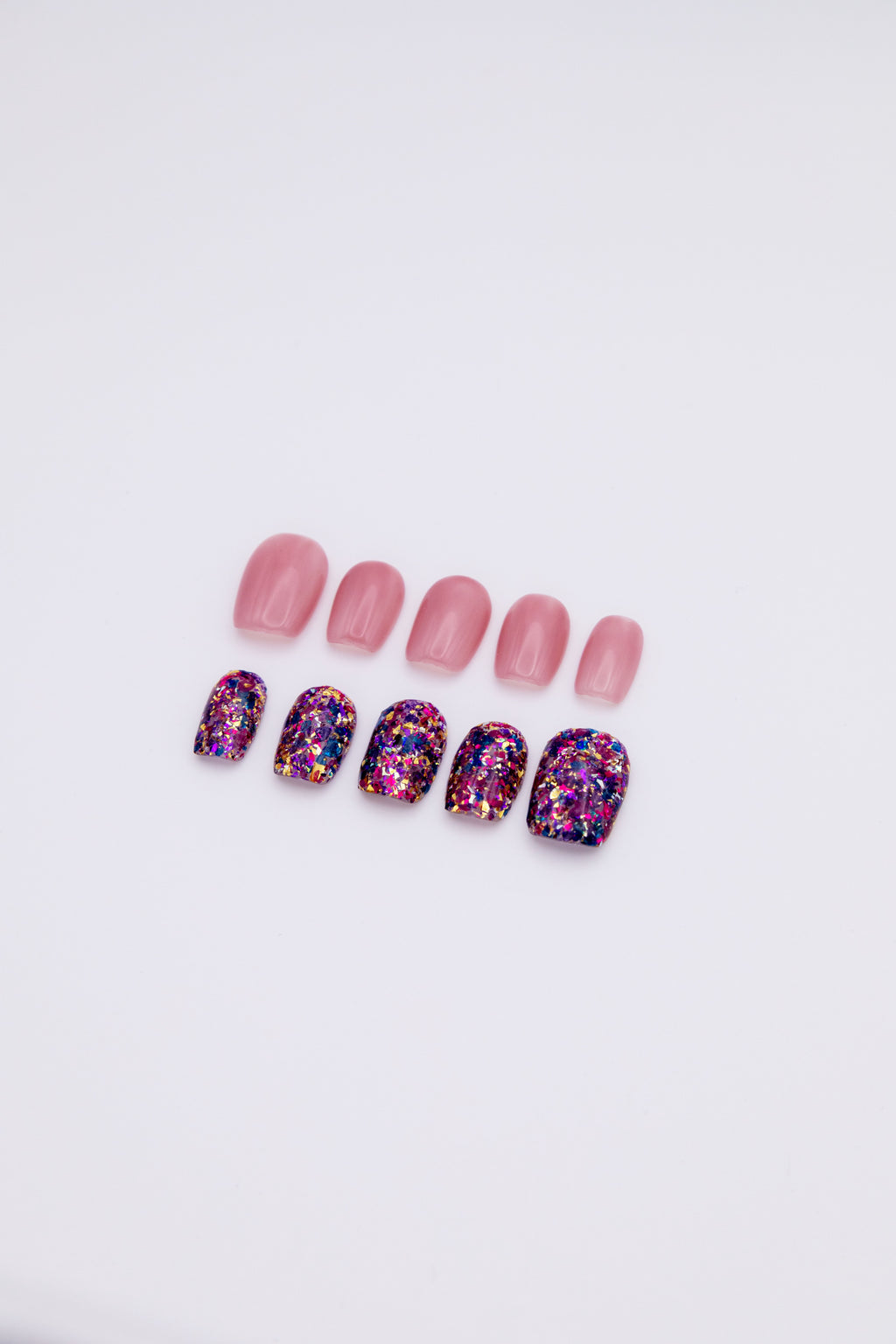Flatlay of 10 short squoval press-on nails showing an asymmetric AB set with sheer jelly pink nails and purple gold galaxy foil glitter nails