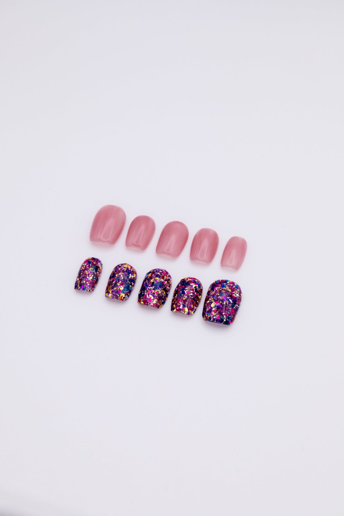 Flatlay of 10 short squoval press-on nails showing an asymmetric AB set with sheer jelly pink nails and purple gold galaxy foil glitter nails