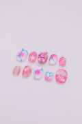 Flatlay of 10 short oval press-on nails featuring vibrant pink and blue aura gradients, Y2K starbursts, glitter, and a cute 3D bunny charm
