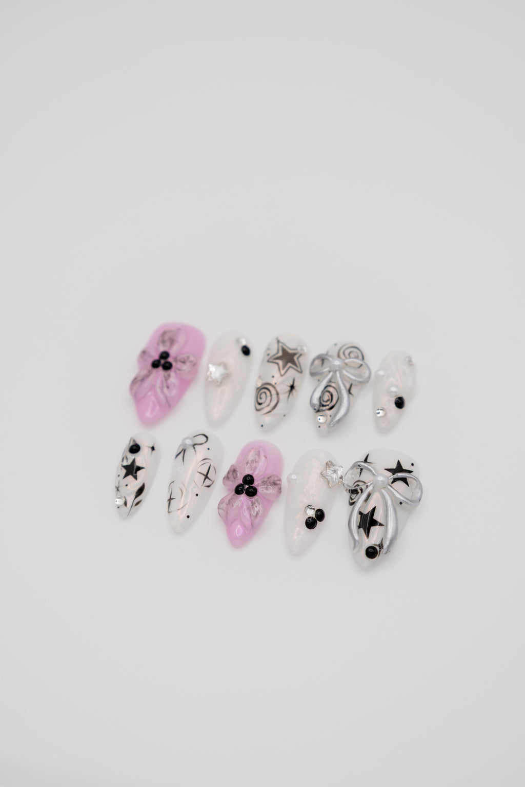 Flatlay of almond press-on nails featuring pink 3D floral designs, silver ribbons, and black Y2K star art