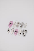 Flatlay of almond press-on nails featuring pink 3D floral designs, silver ribbons, and black Y2K star art