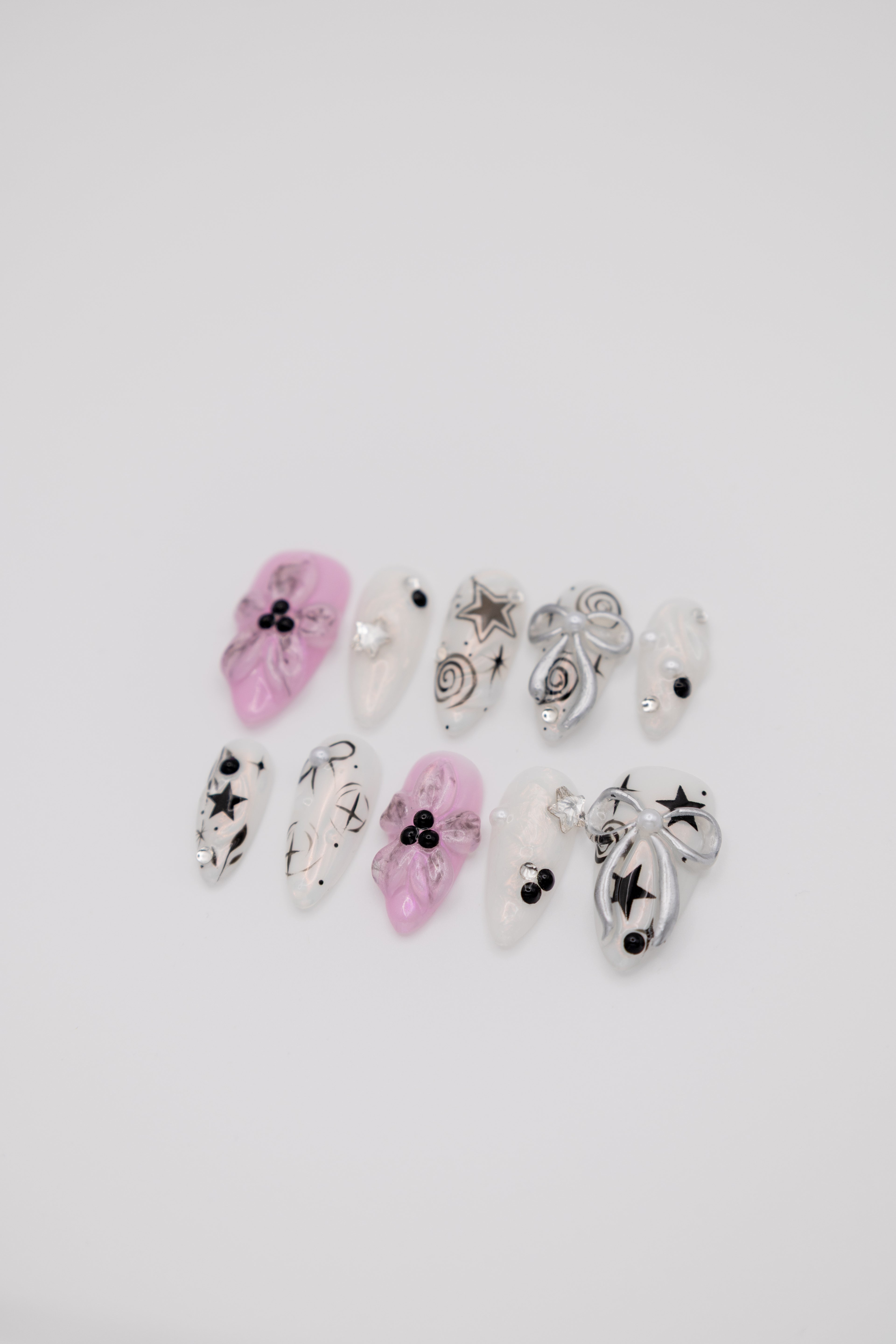 Flatlay of almond press-on nails featuring pink 3D floral designs, silver ribbons, and black Y2K star art
