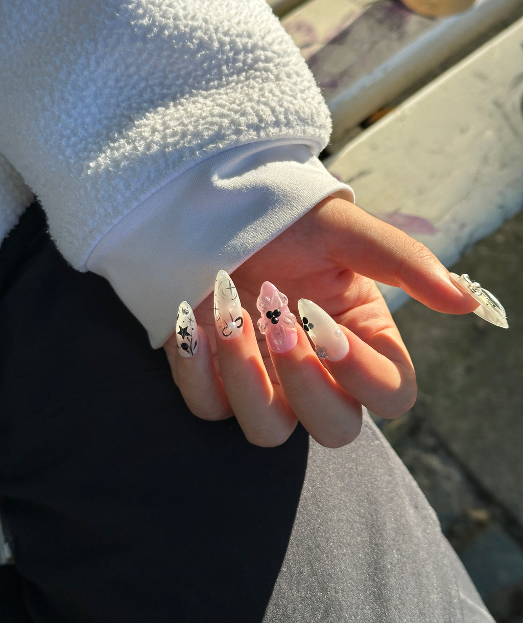 Hand wearing Cyber Coquette almond press-on nails in natural outdoor sunlight, showing 3D pink gel flowers and silver metallic Y2K star details