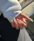 Hand wearing Cyber Coquette almond press-on nails in natural outdoor sunlight, showing 3D pink gel flowers and silver metallic Y2K star details