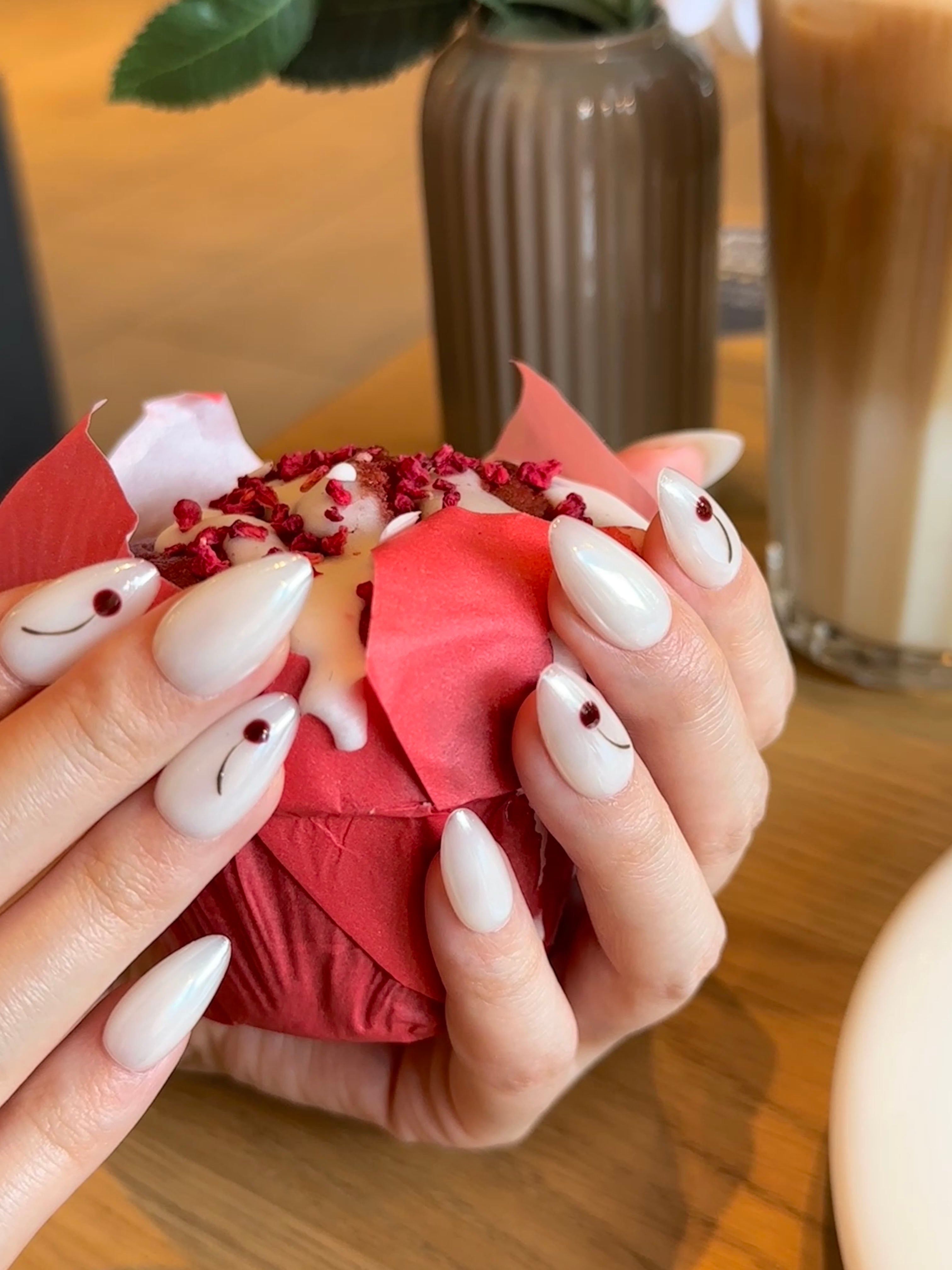 Lifestyle photo of Frost Berry almond press-on nails worn on a hand holding a drink outdoors, showing reusable pearlescent white tips with berry accents.