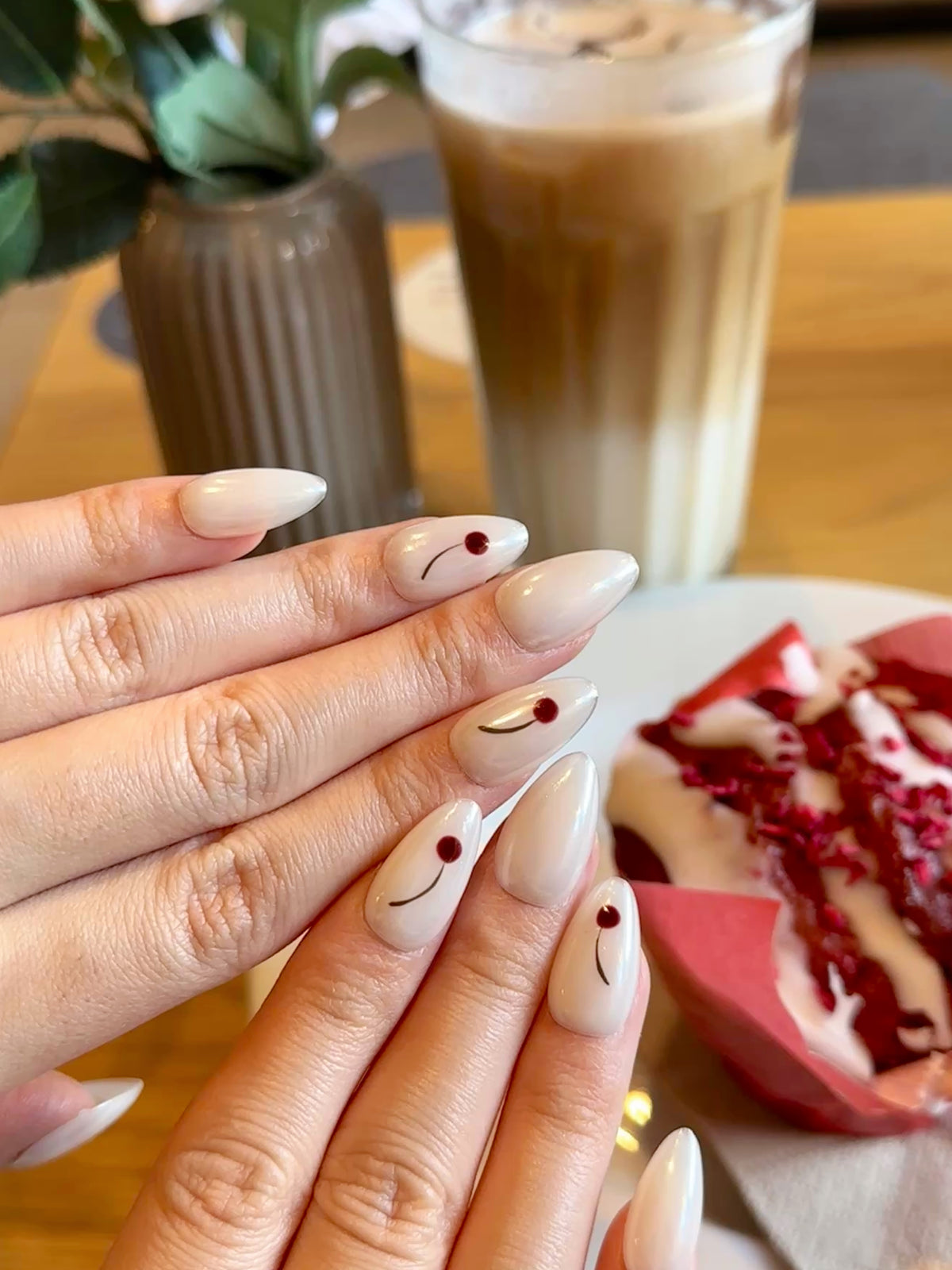 Close-up of Frost Berry almond press-on nails on a hand, showing pearlescent white finish and minimalist burgundy berry nail art.