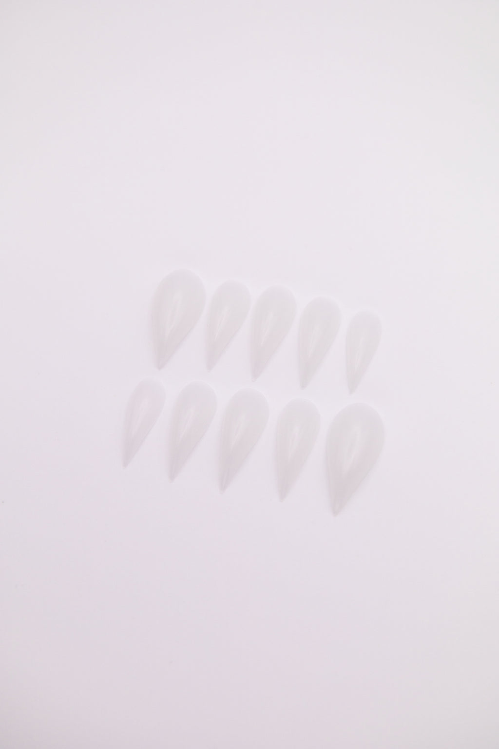 Flatlay of 10 Frost Dragon Claw shaped press-on nails with translucent icy milky clear finish on a plain white background