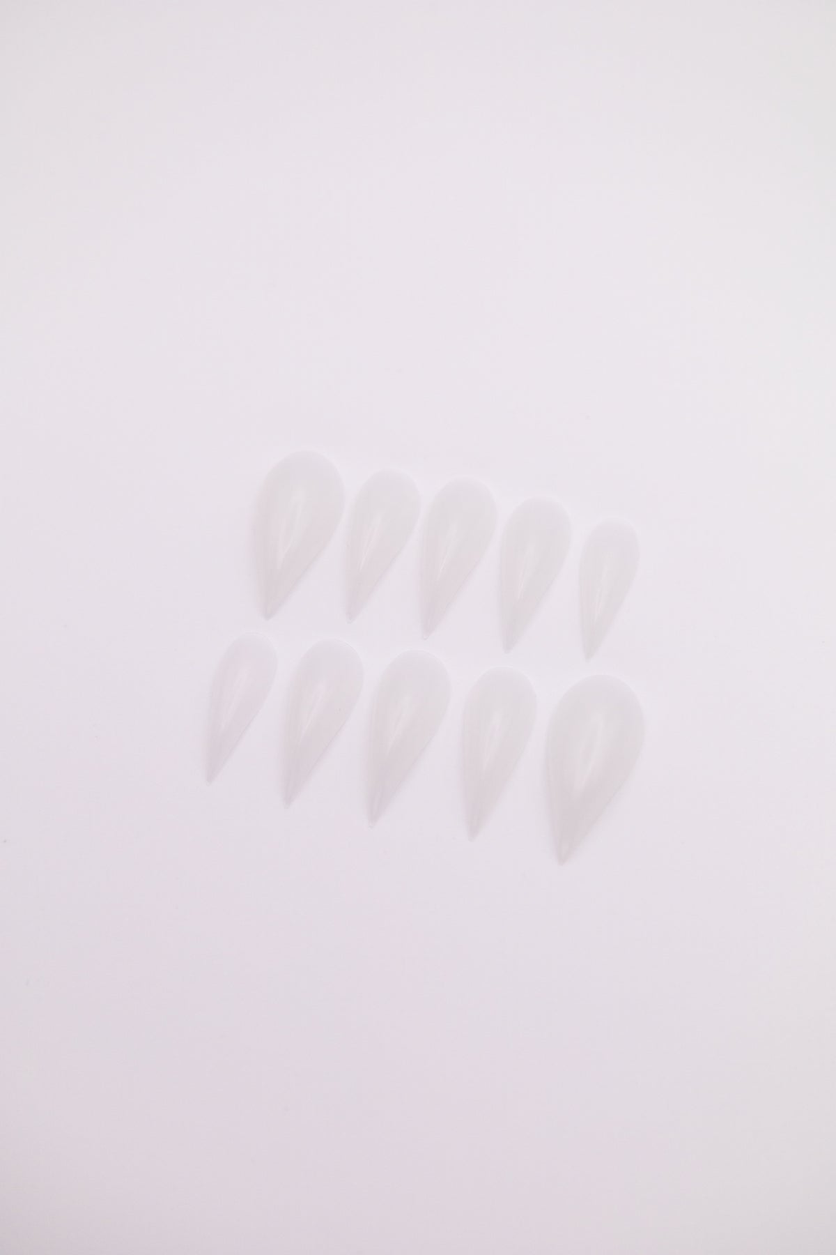 Flatlay of 10 Frost Dragon Claw shaped press-on nails with translucent icy milky clear finish on a plain white background