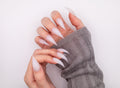 Close-up of hands with grey knit sleeves wearing dramatic translucent milky Frost Dragon Claw press-on nails posed in a sharp claw curve