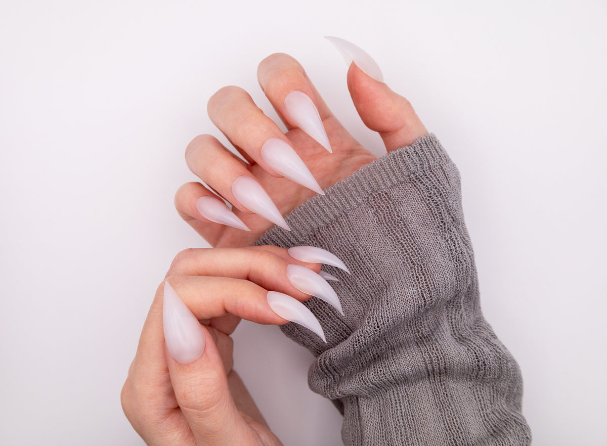 Close-up of hands with grey knit sleeves wearing dramatic translucent milky Frost Dragon Claw press-on nails posed in a sharp claw curve