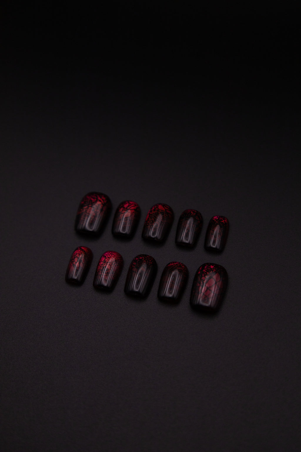 Flatlay of 10 medium squoval glossy burgundy press-on nails with black lace patterns on a black background