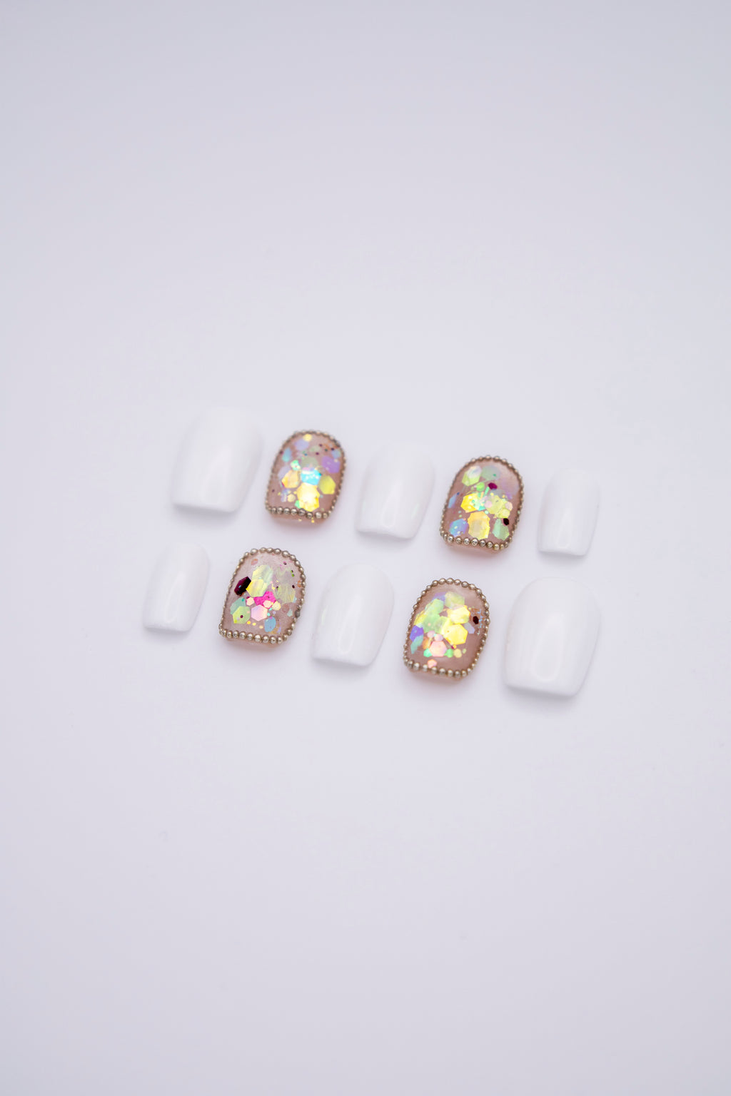 Flatlay of 10 short squoval press-on nails featuring solid milky white nails and iridescent chunky sequins with tiny bead borders