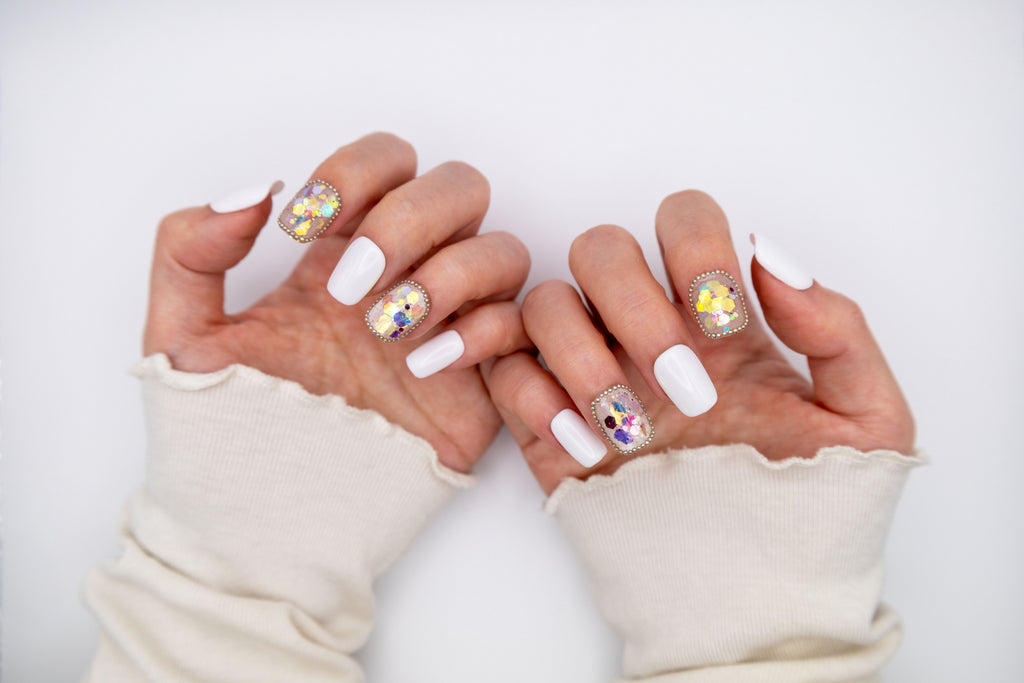 Close-up of hands wearing creamy sweater sleeves displaying milky white press-on nails with sparkling iridescent sequin accents