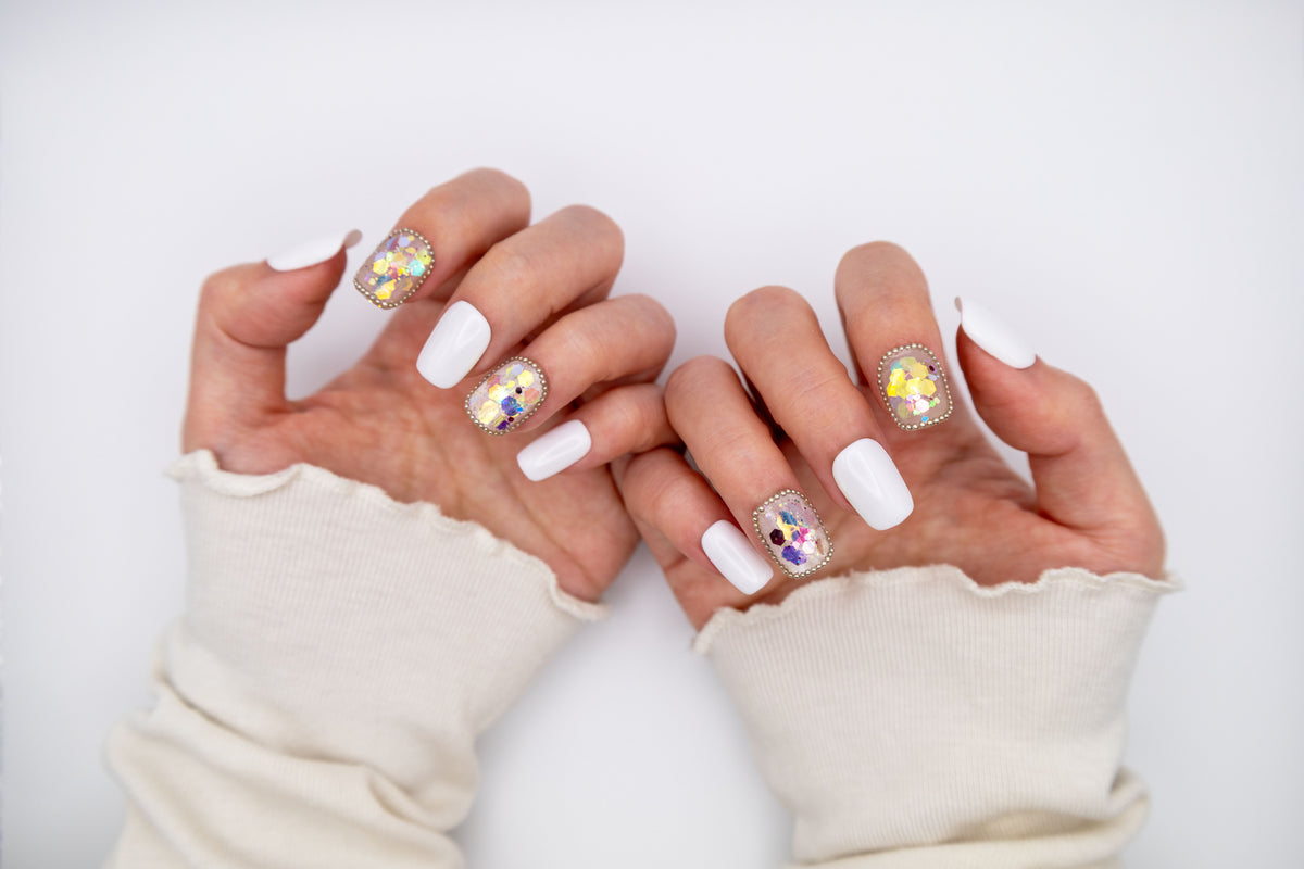 Close-up of hands wearing creamy sweater sleeves displaying milky white press-on nails with sparkling iridescent sequin accents