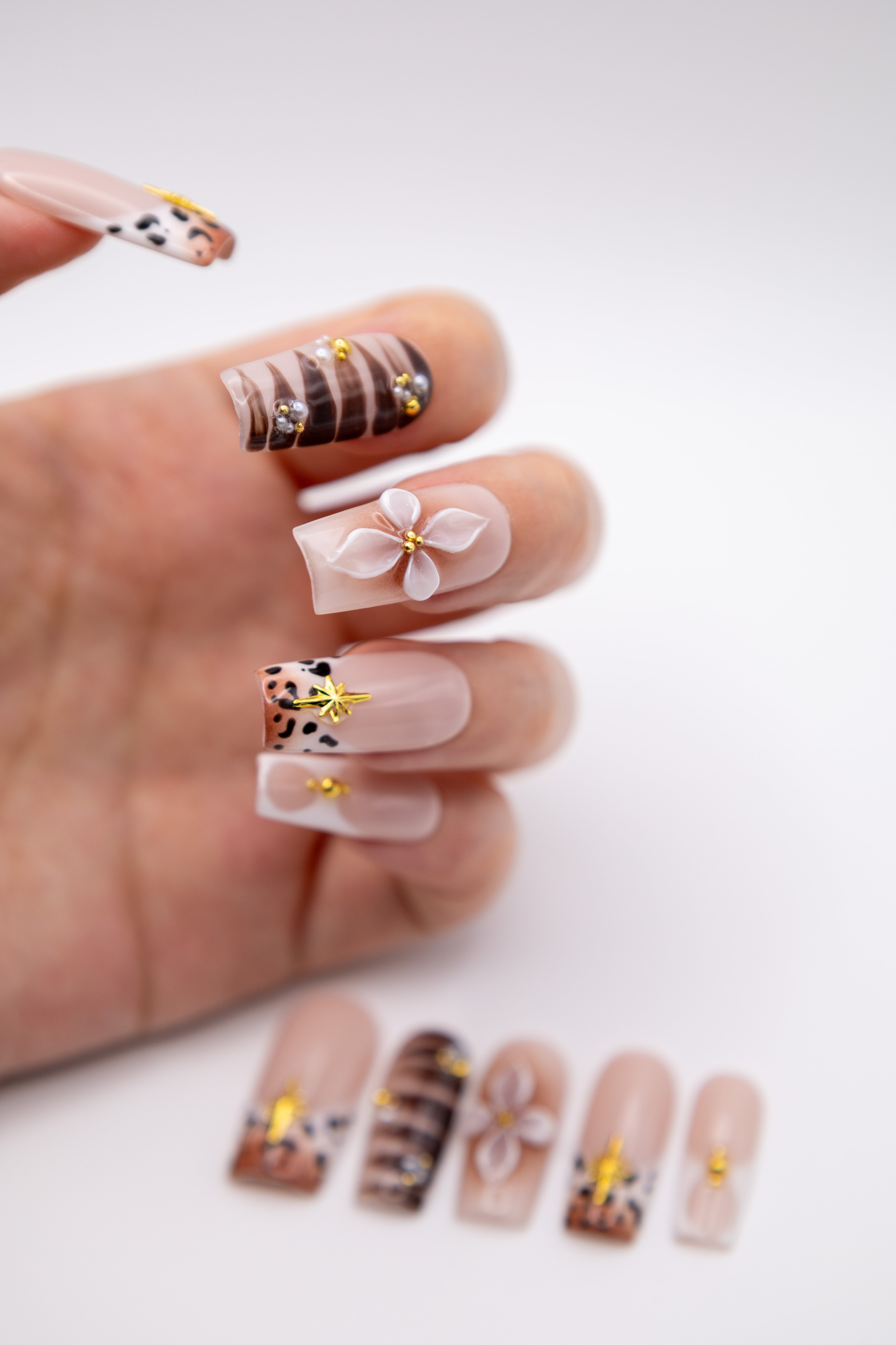 Hand showing luxury coffin press-on nails featuring 3D sculpted flower art, leopard print tips, and pearls