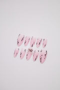 Flatlay of matte pink white gradient almond press-on nails featuring black ink strokes and a 3D floral charm