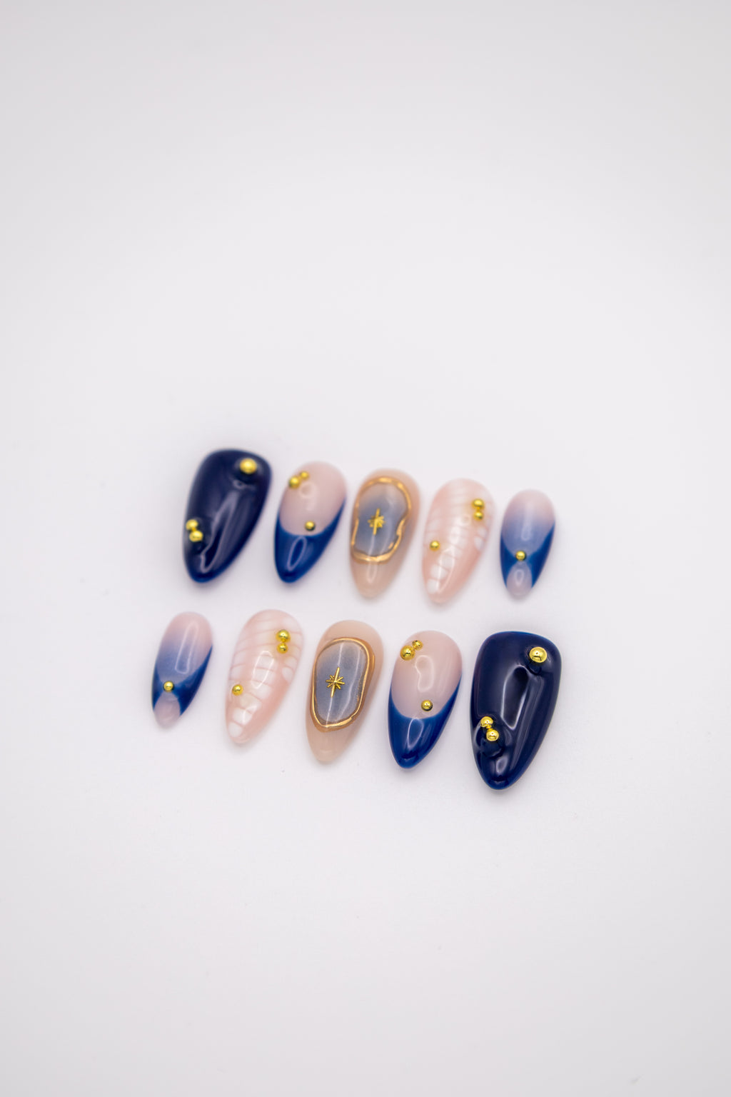 Flatlay of deep blue blush almond press-on nails featuring 3D white relief texture and gold celestial frames