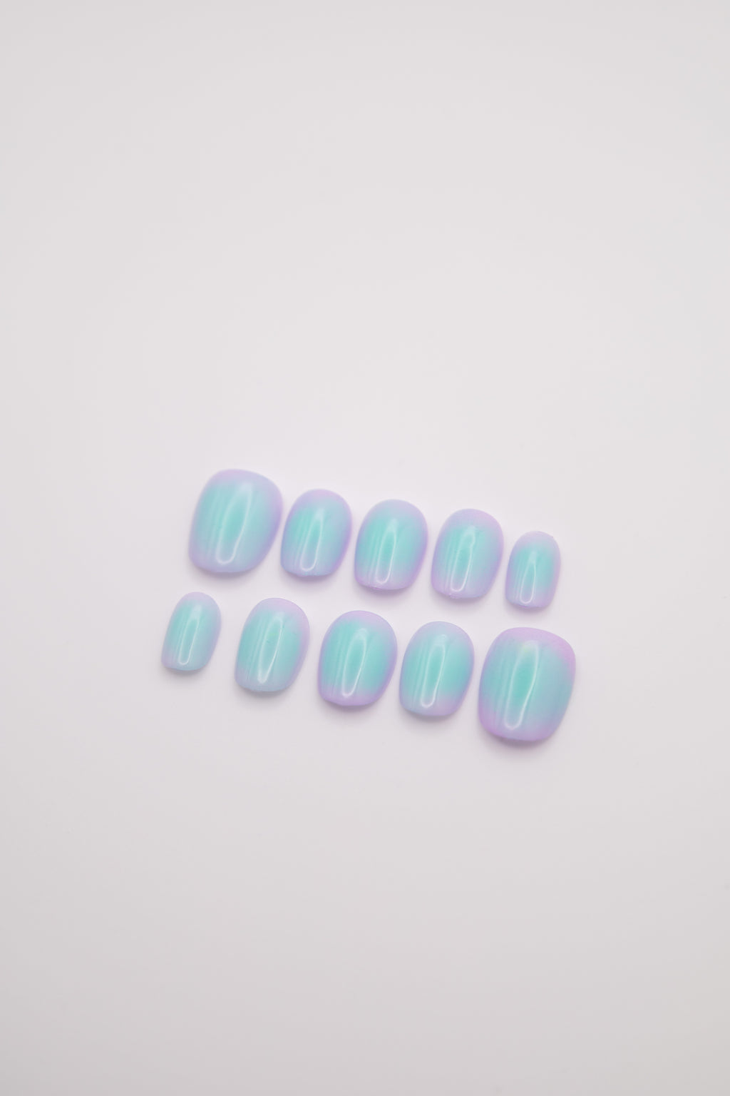 Flatlay of short square press-on nails featuring a glossy lavender and mint green blush aura gradient