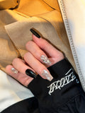 Hand wearing Night Shimmer long coffin press-on nails with silver starburst designs, rhinestones, and black accent nails.