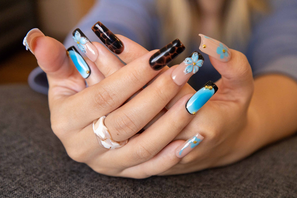 Close-up of hands displaying glossy coffin press-on nails featuring 3D blue flowers, tortoiseshell pattern, and azure aura blush