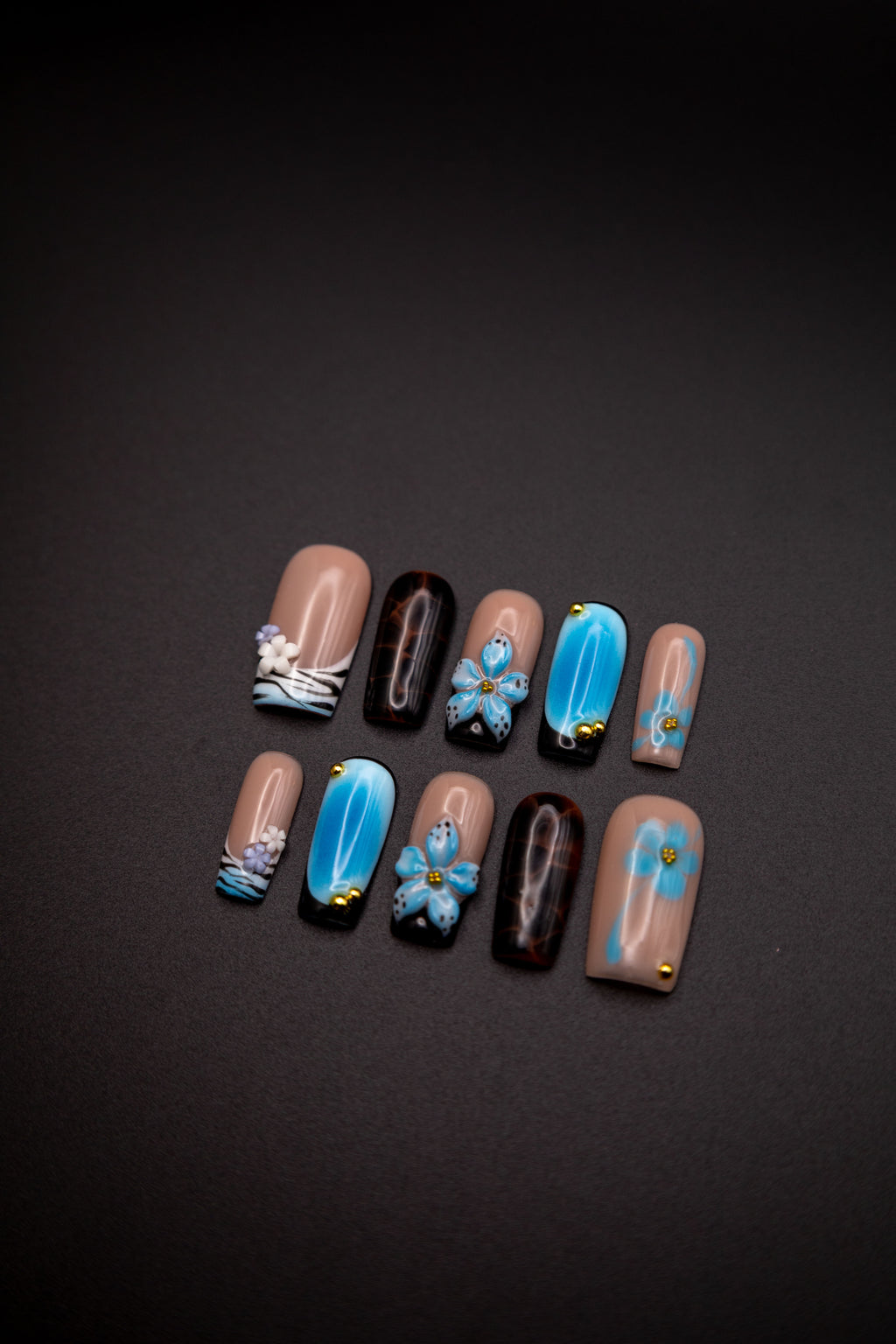 Flatlay of coffin press-on nails featuring blue aura blush, 3D blue flowers, dark tortoiseshell pattern, and gold beads