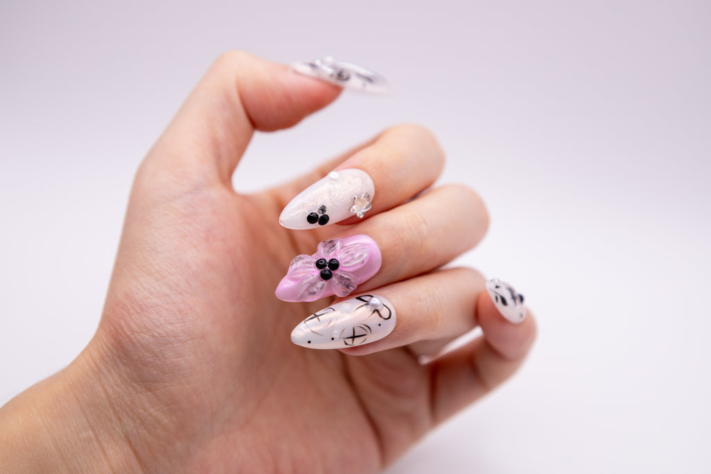 Hand showing glossy pink and silver press-on nails with 3D sculpted flower, pearls, and black celestial motifs