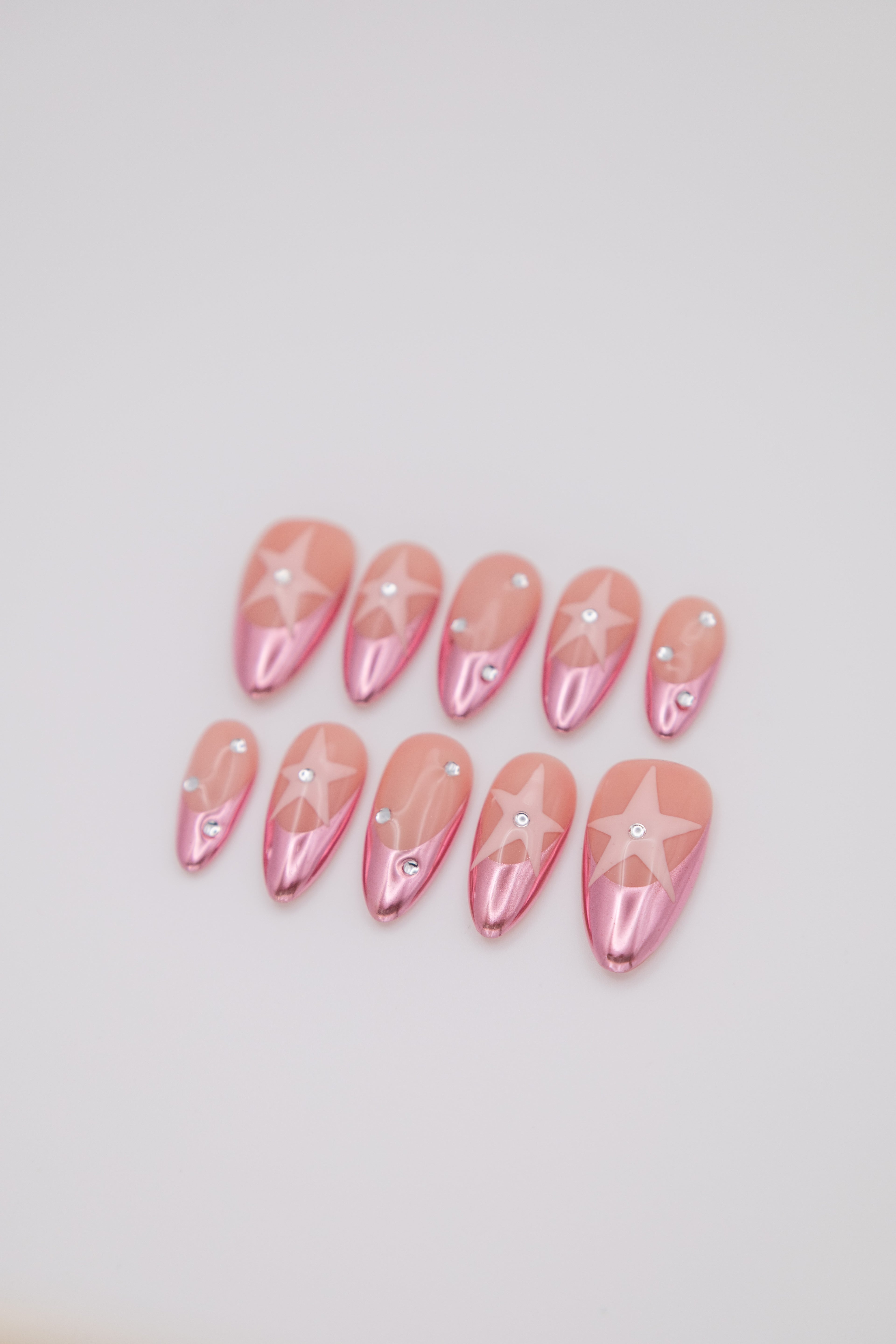 Flatlay of metallic pink chrome almond press-on nails featuring star designs and rhinestone accents