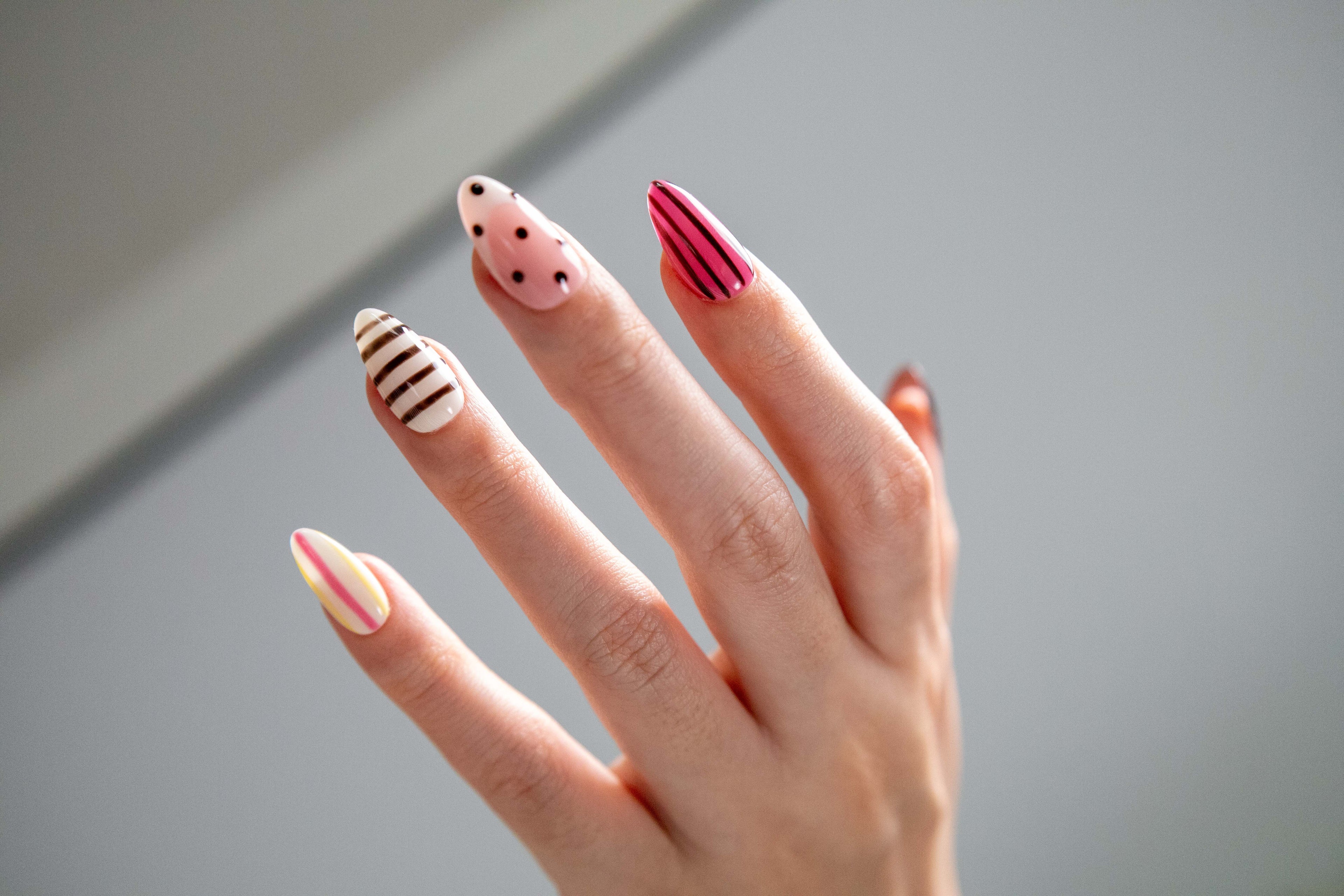 Hand raised against bright light showing playful pink and black striped polka dot press-on nails