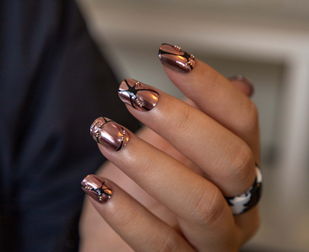 Hand showing metallic rose bronze chrome short press-on nails with 3D black organic line designs