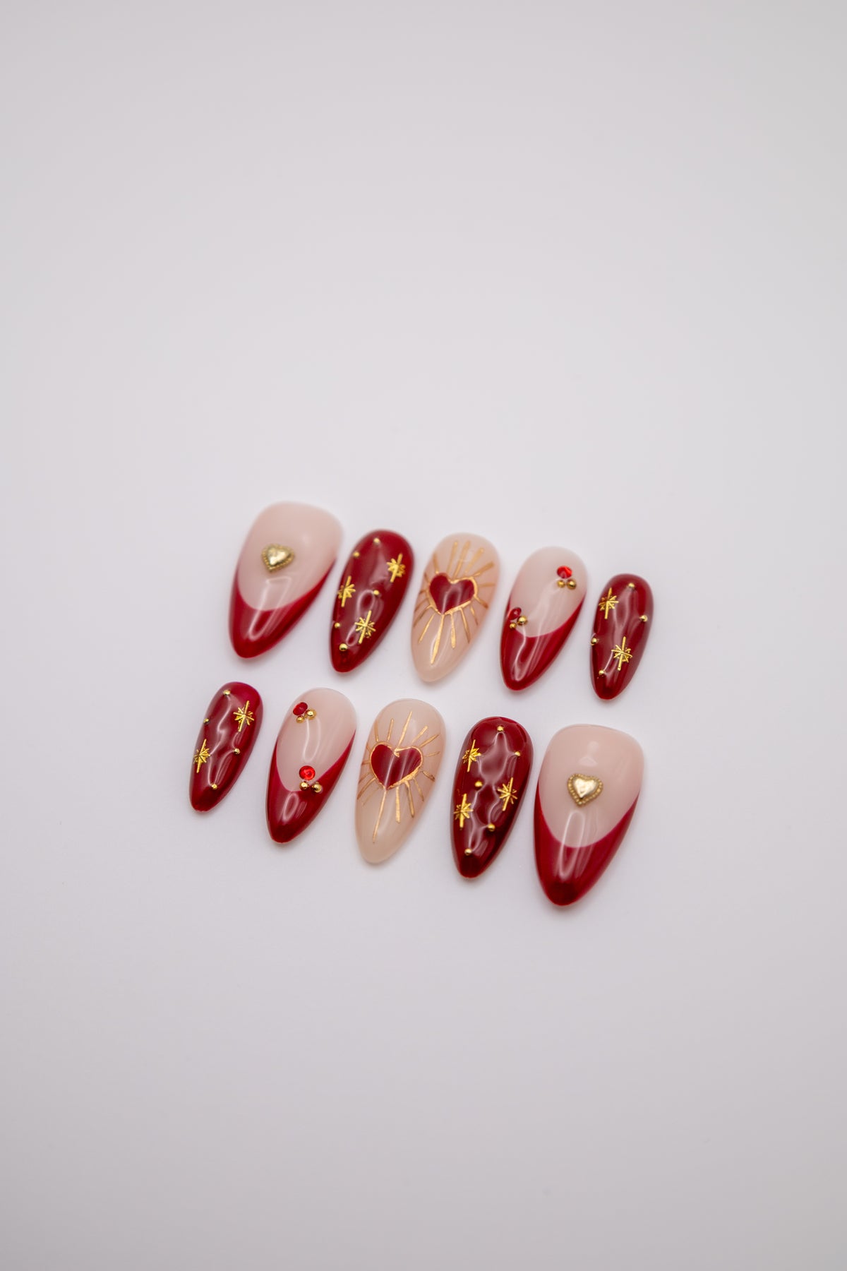 Flatlay of glossy red and nude almond press-on nails featuring gold celestial starbursts and heart designs