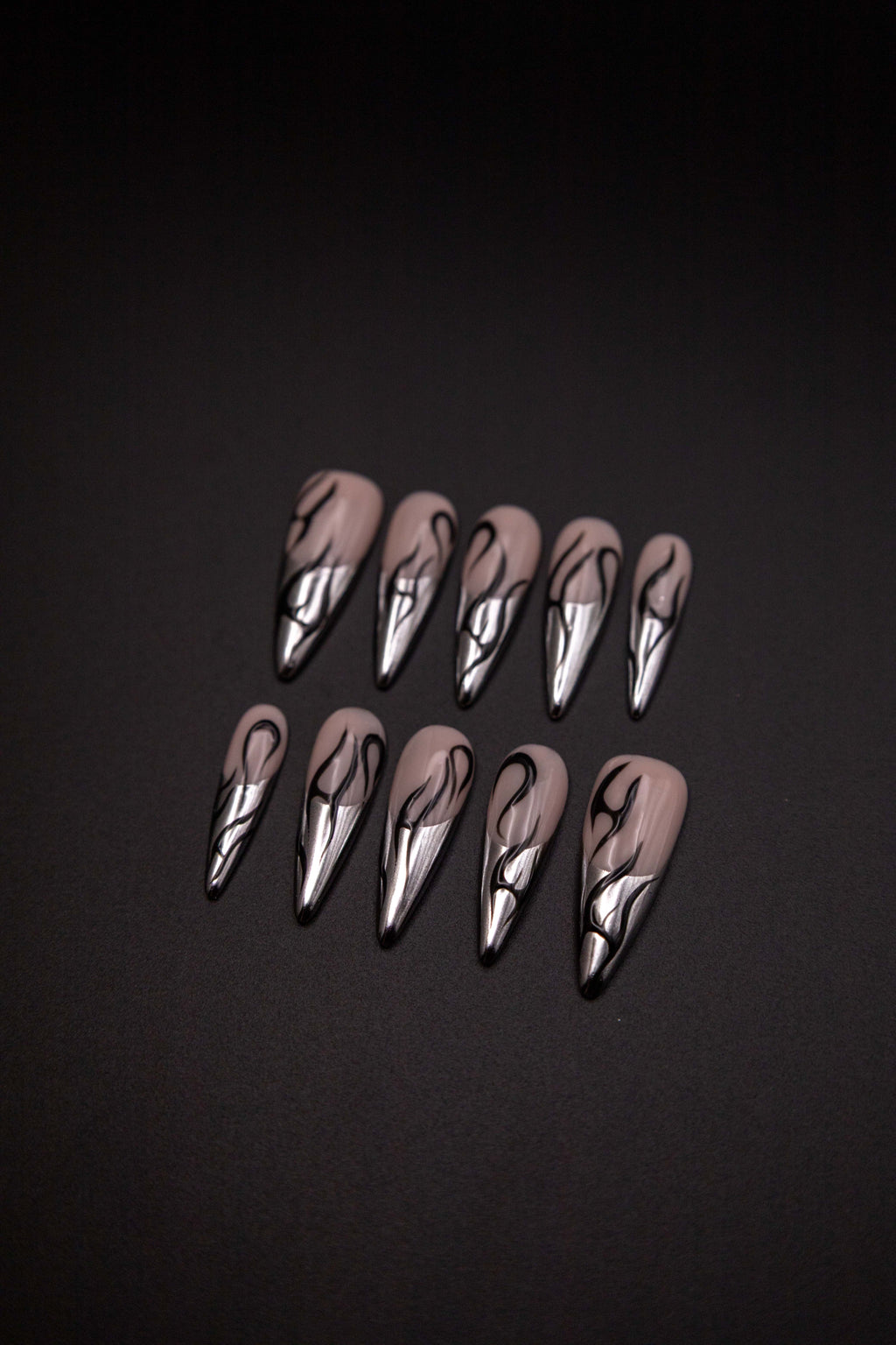 Flatlay of long almond press-on nails featuring liquid silver chrome French tips and black tribal flame line art