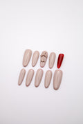 Flatlay of taupe nude almond press-on nails featuring a 3D cross charm and a hidden crimson red underside