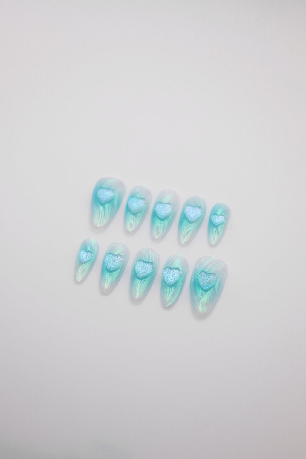 Tide Glow teal water ripple almond press-on nails set with 3D heart charms flatlay