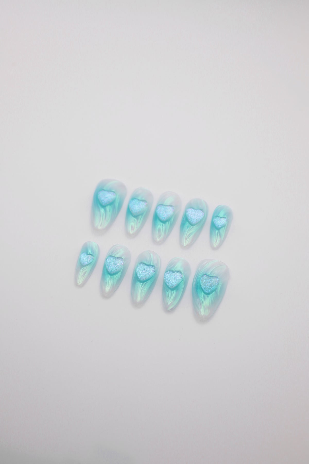 Tide Glow teal water ripple almond press-on nails set with 3D heart charms flatlay