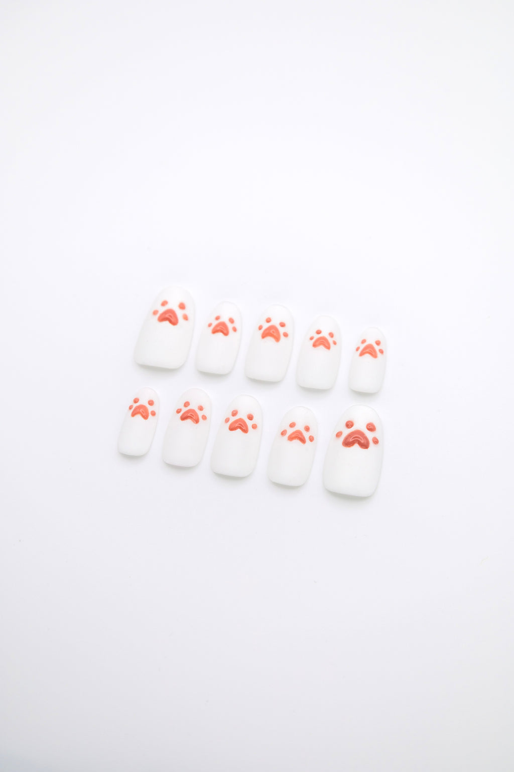 Flatlay of 10 short squoval press-on nails featuring sparkling diamond dust white base with glossy 3D pink cat paw details