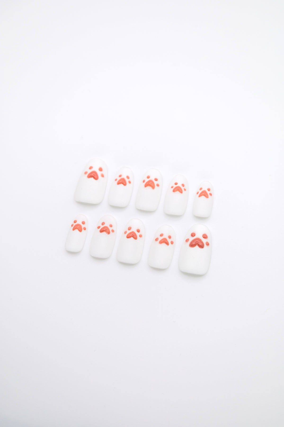 Flatlay of 10 short squoval press-on nails featuring sparkling diamond dust white base with glossy 3D pink cat paw details