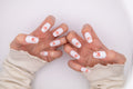Close-up of hands posing like cute cat paws wearing diamond dust sparkly white press-on nails with 3D pink paw bean accents