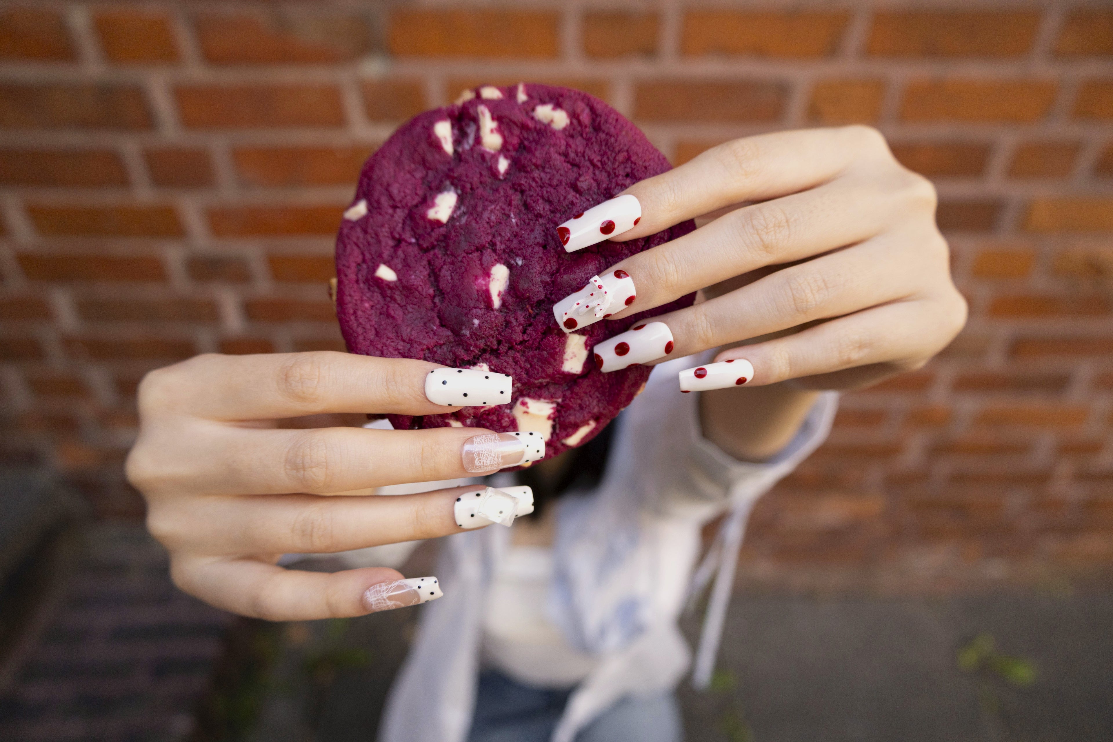 Close-up of vintage polka dot and bow accent press-on nails in natural light with a cookie