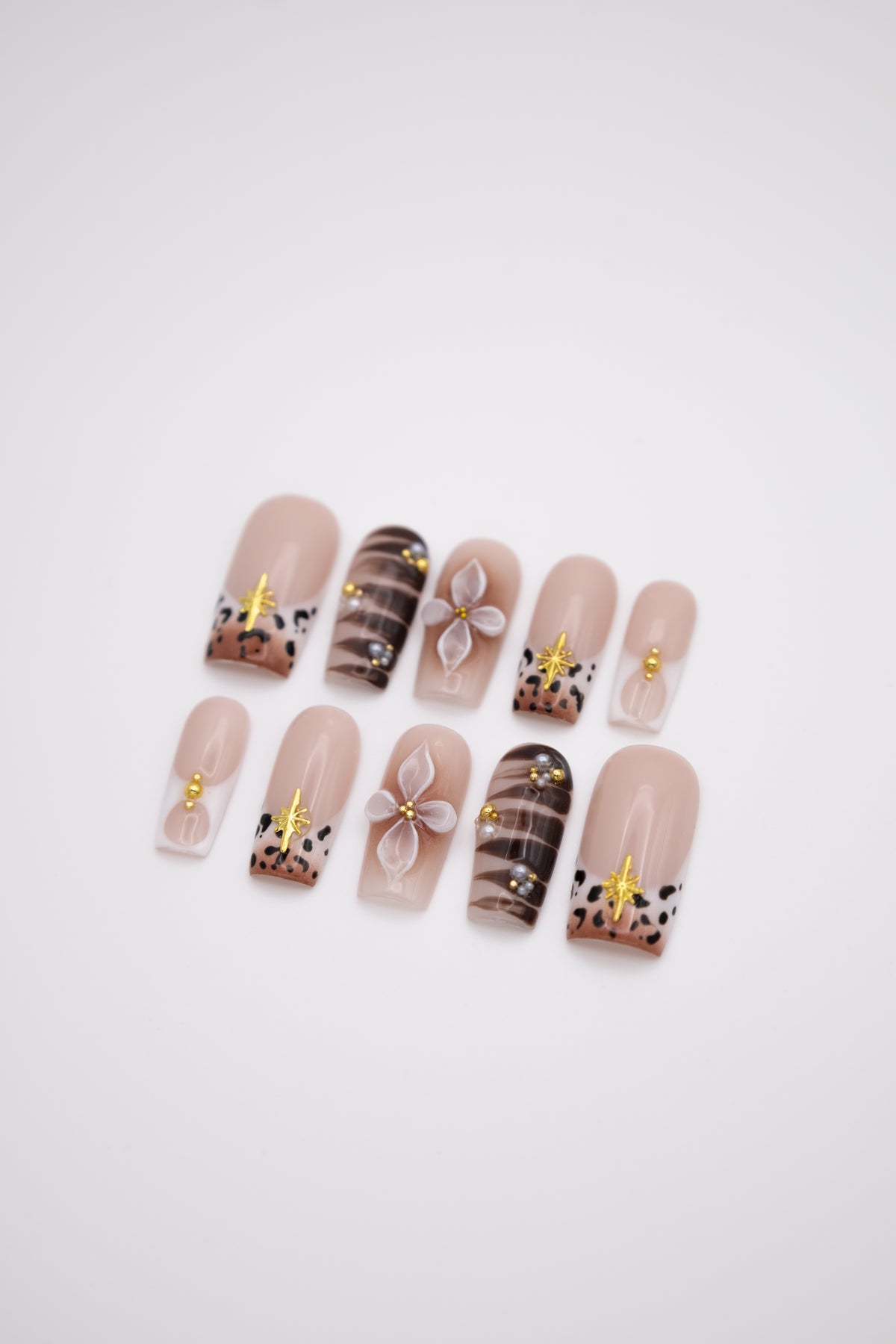 Flatlay of nude coffin press-on nails with brown leopard print french tips, 3D white flowers, and gold stars