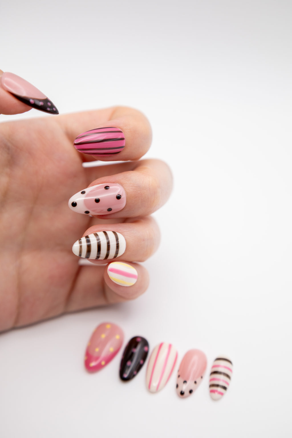 Close-up of hand showing Y2K style almond press-on nails with retro dots and stripe pattern mix