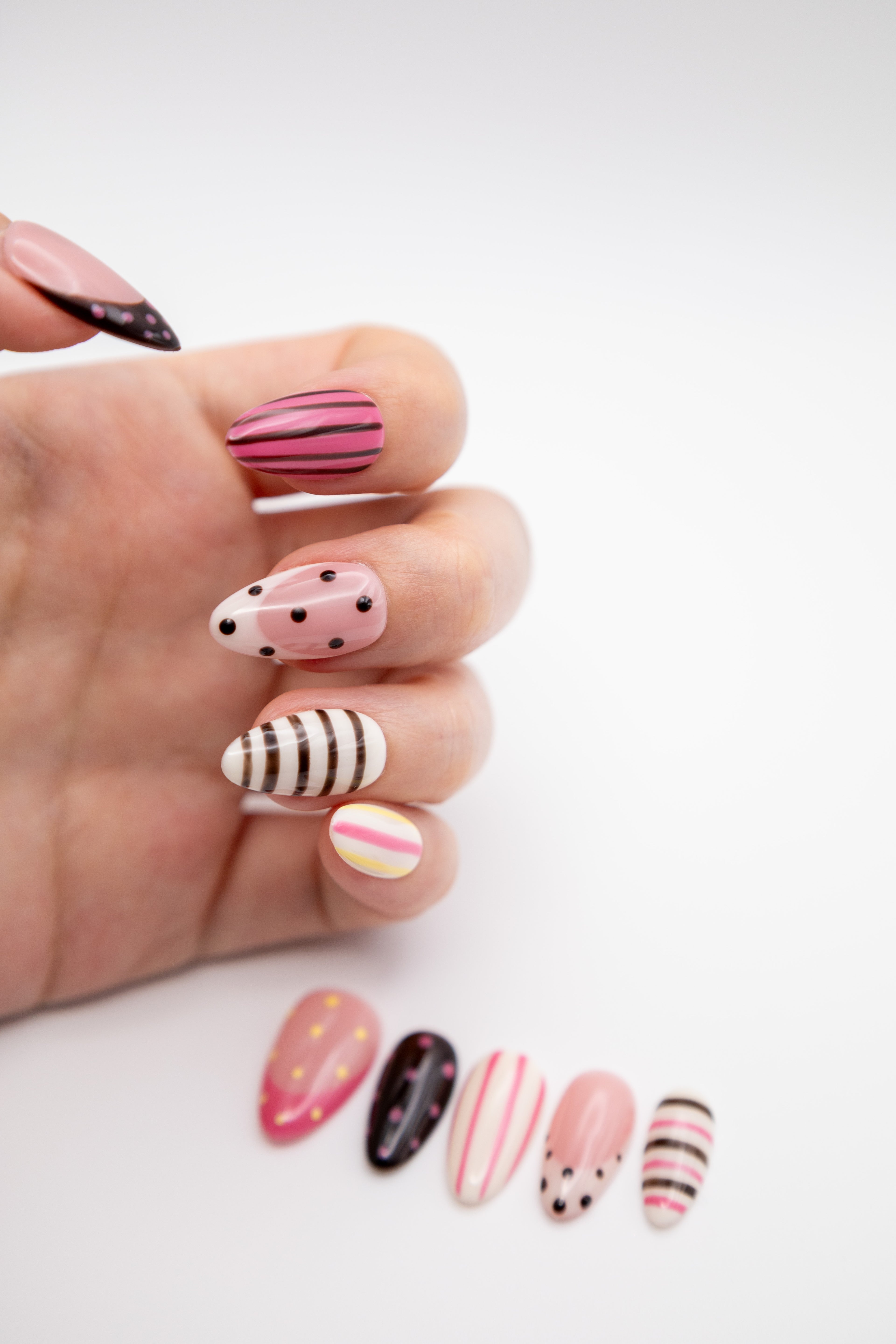 Close-up of hand showing Y2K style almond press-on nails with retro dots and stripe pattern mix