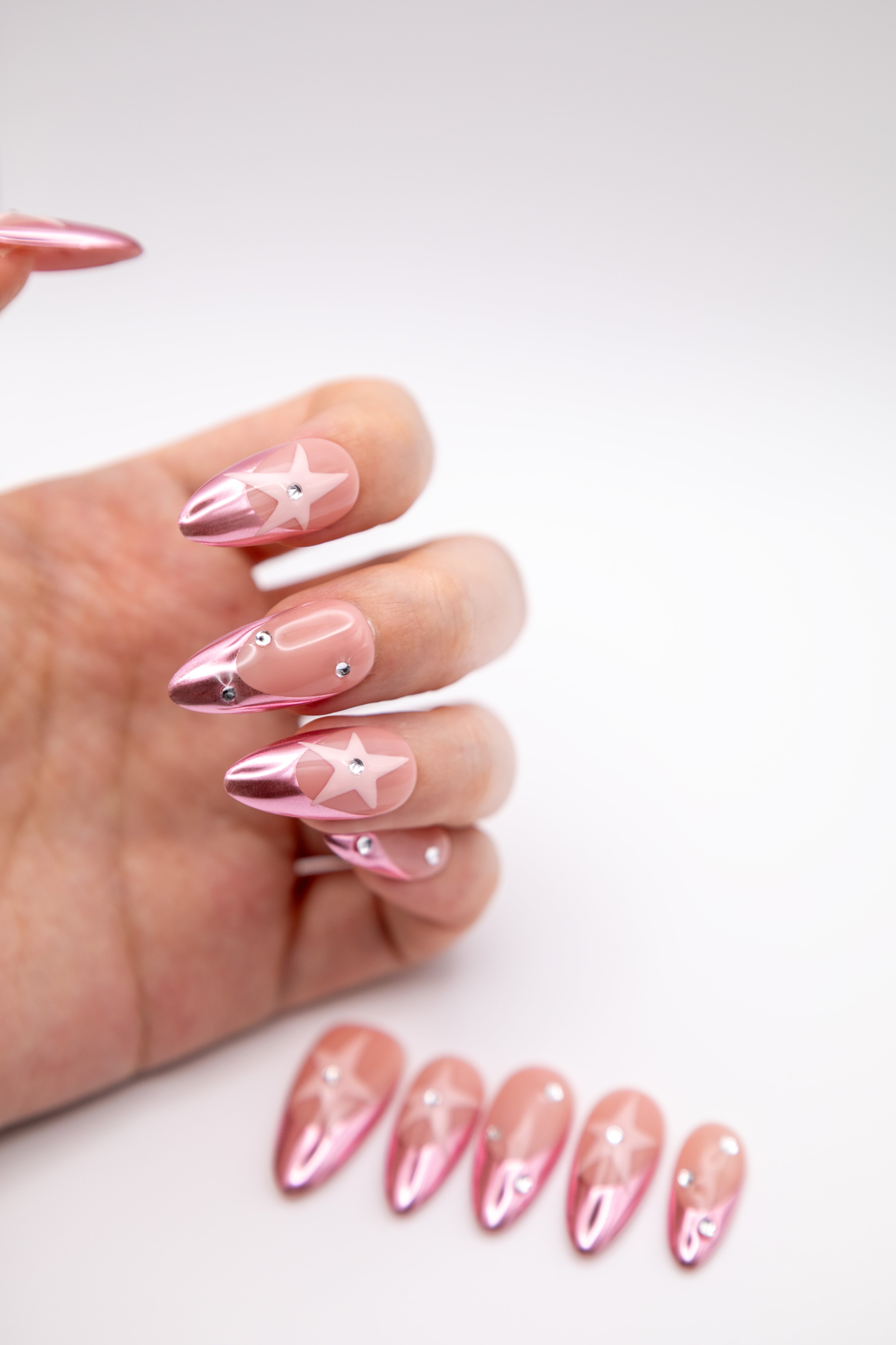 Hand showing Y2K glossy metallic pink chrome press-on nails with stars and sparkling crystals